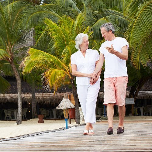 Pareja mayor caminando sobre un muelle de madera cogidos de la mano mirándose el uno al otro